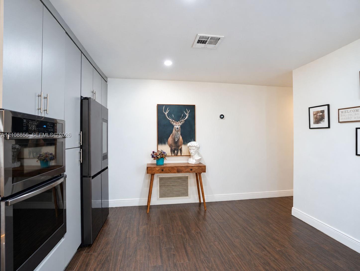 Floor-to-ceiling flat-panel cabinetry, integrated stainless steel double oven, stainless steel multi-door refrigerator, and wood-finish flooring