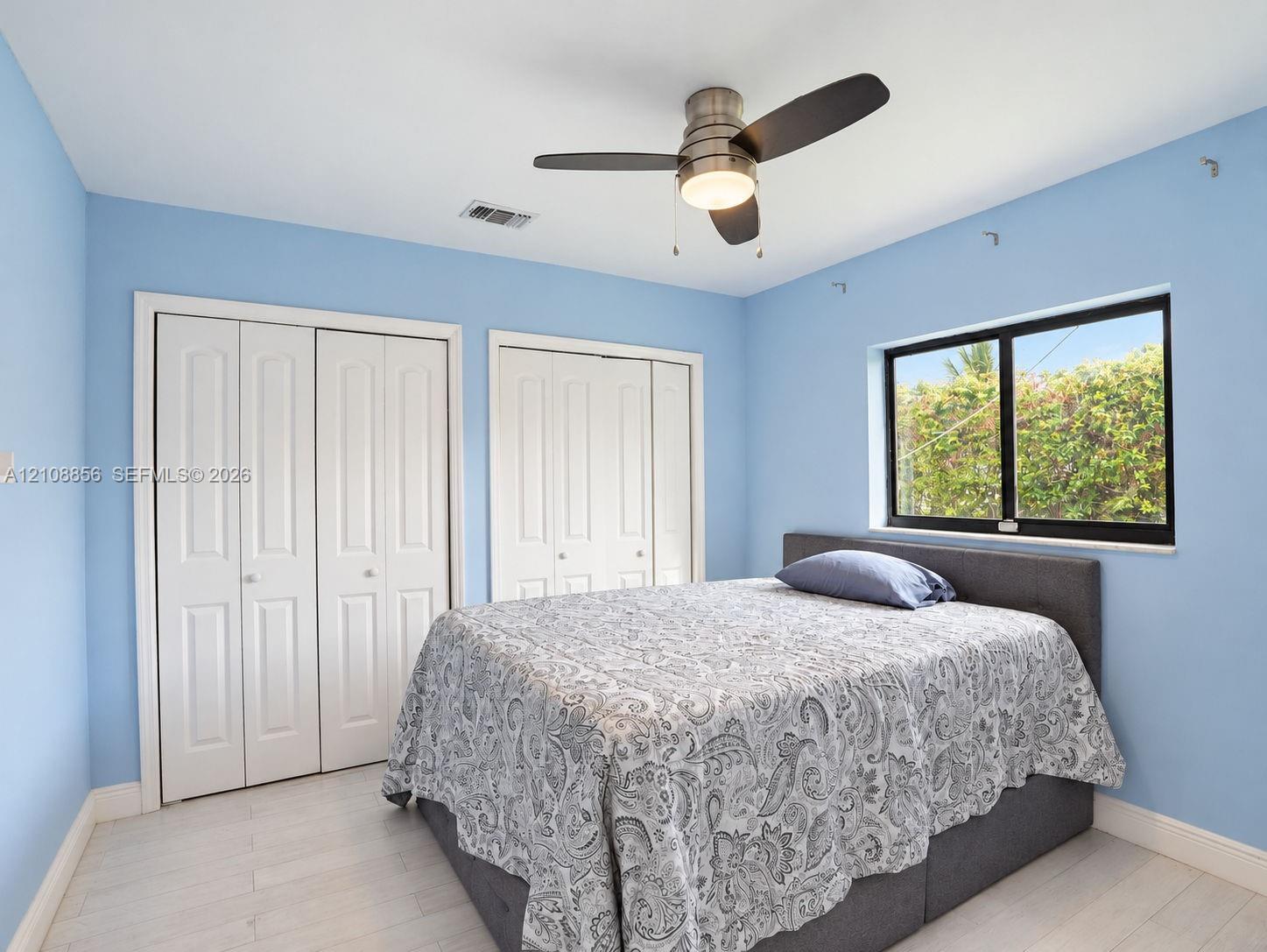 Light-filled room featuring wood-finish flooring, two sets of white bi-fold closet doors, and a brushed nickel ceiling fan with integrated lighting