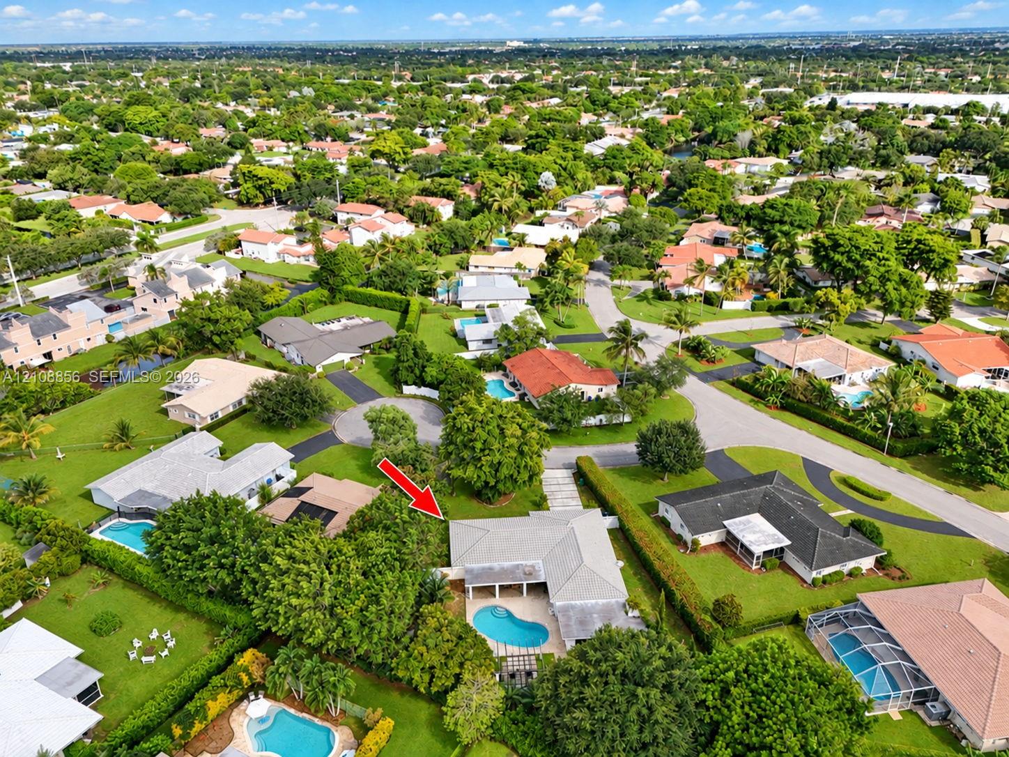 Aerial perspective of a single-story residence featuring a private swimming pool, concrete patio, hipped roofline, and mature landscaping