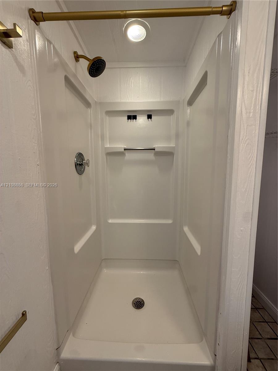Shower stall with white molded surround, built-in shelving, brass-finish shower head, and recessed ceiling lighting