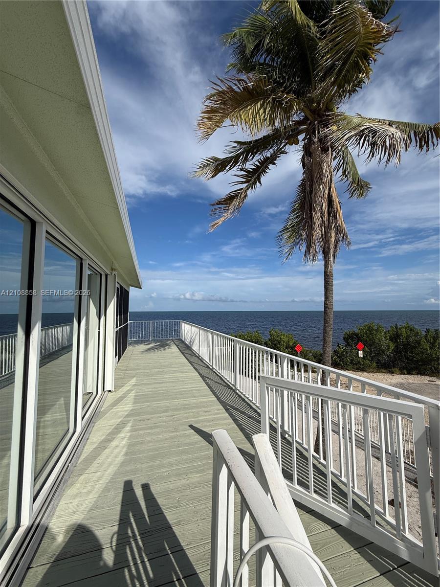 Extended deck featuring composite planking, white metal railings, sliding glass exterior doors, and a waterfront location Extended deck featuring composite planking, white metal railings, sliding glass exterior doors, and a waterfront location