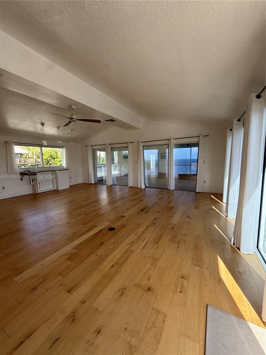 Spacious interior featuring wood-finish flooring, vaulted ceilings, multiple sliding glass doors, a ceiling fan, and built-in cabinetry with a countertop Spacious interior featuring wood-finish flooring, vaulted ceilings, multiple sliding glass doors, a ceiling fan, and built-in cabinetry with a countertop