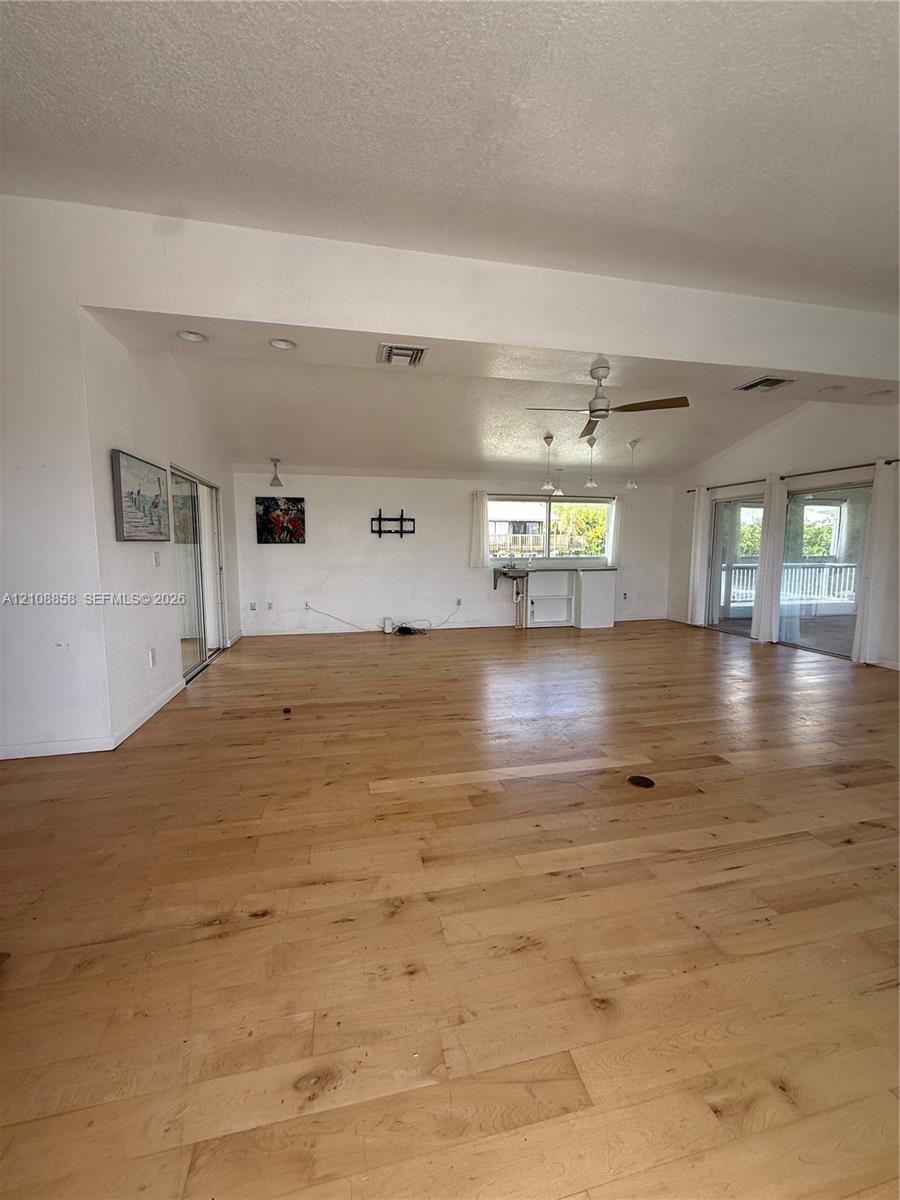 Open-concept living space featuring wood-finish flooring, vaulted ceilings, recessed lighting, a ceiling fan, and sliding glass doors Open-concept living space featuring wood-finish flooring, vaulted ceilings, recessed lighting, a ceiling fan, and sliding glass doors