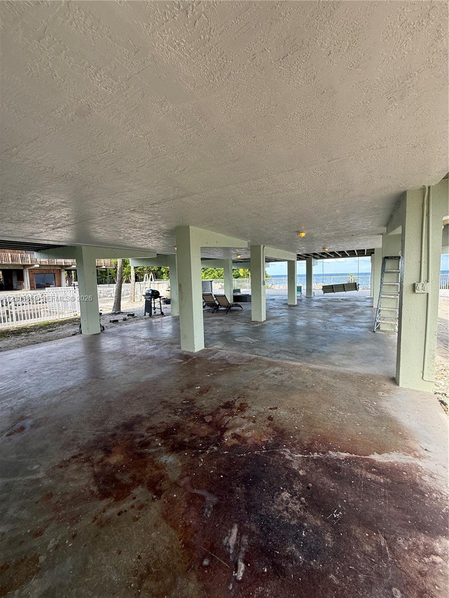 Elevated foundation featuring reinforced concrete structural supports, expansive covered hardscaping, and water frontage