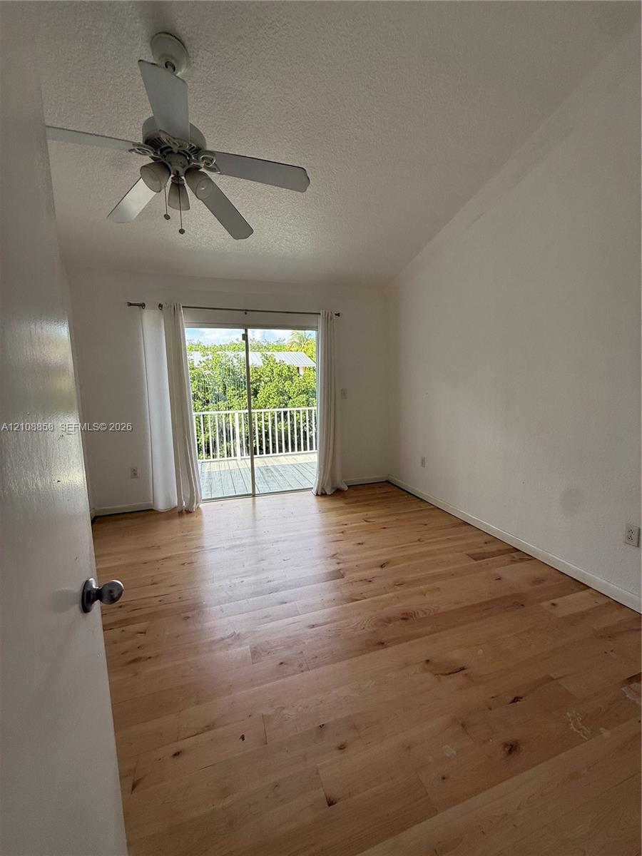 Vaulted ceilings, wood-finish flooring, ceiling fan with integrated lighting, and sliding glass doors with balcony access