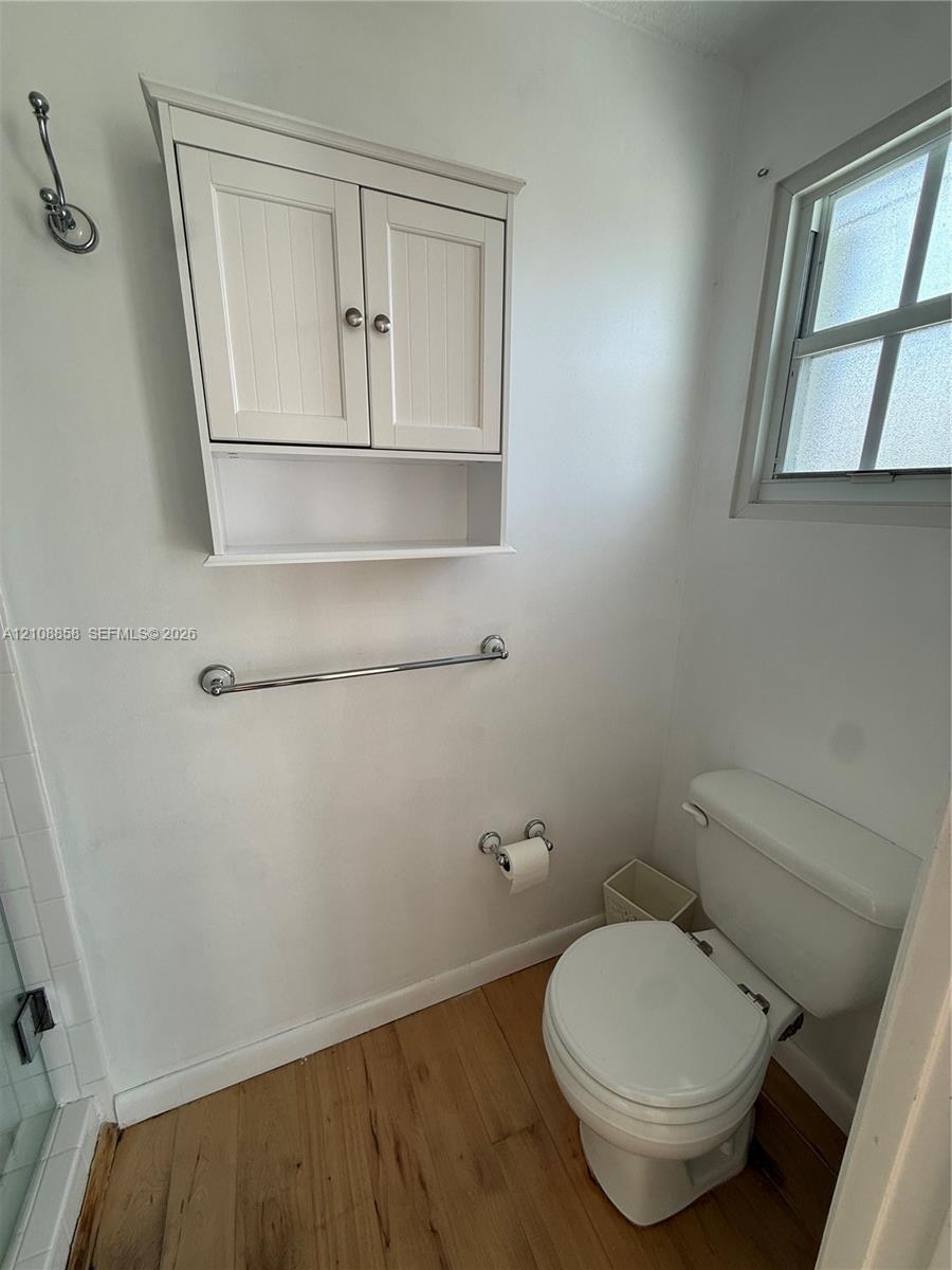 Wall-mounted white shaker-style cabinet with open shelving, wood-finish flooring, and multi-pane window