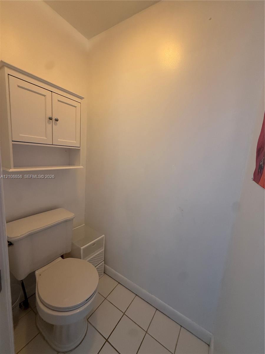 White wall-mounted cabinetry featuring shaker-style doors, an open lower shelf, and ceramic tile flooring