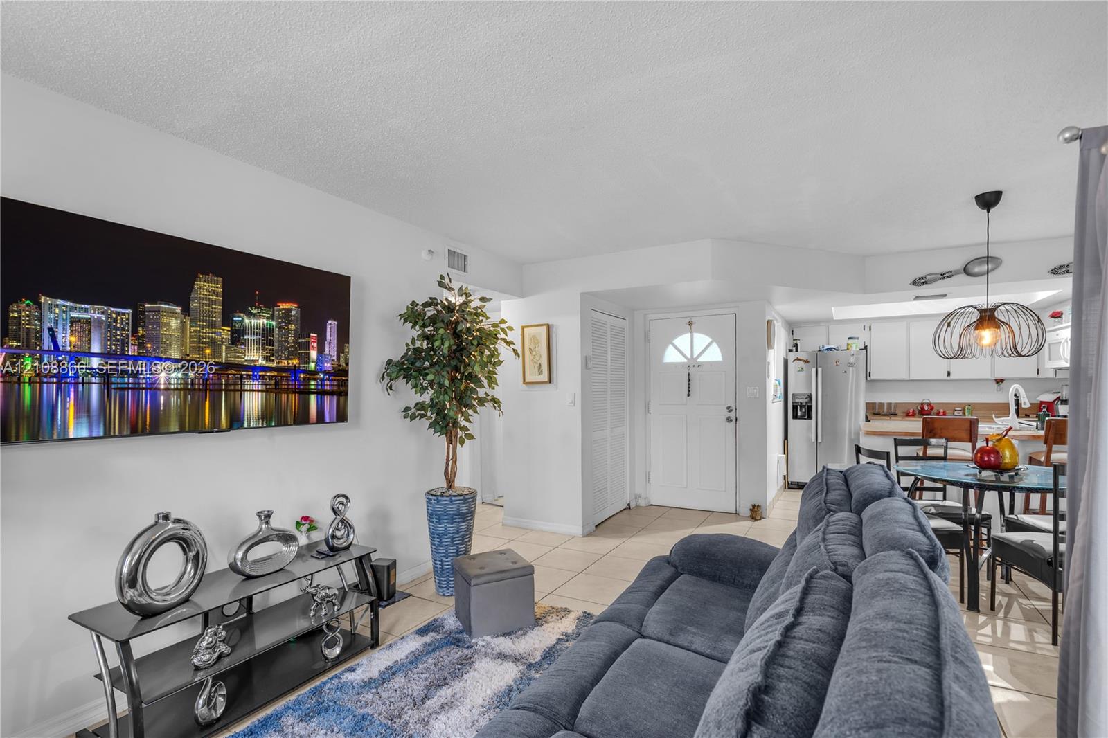 Open-concept area featuring neutral tile flooring, white cabinetry, a kitchen island, and a distinctive pendant light fixture