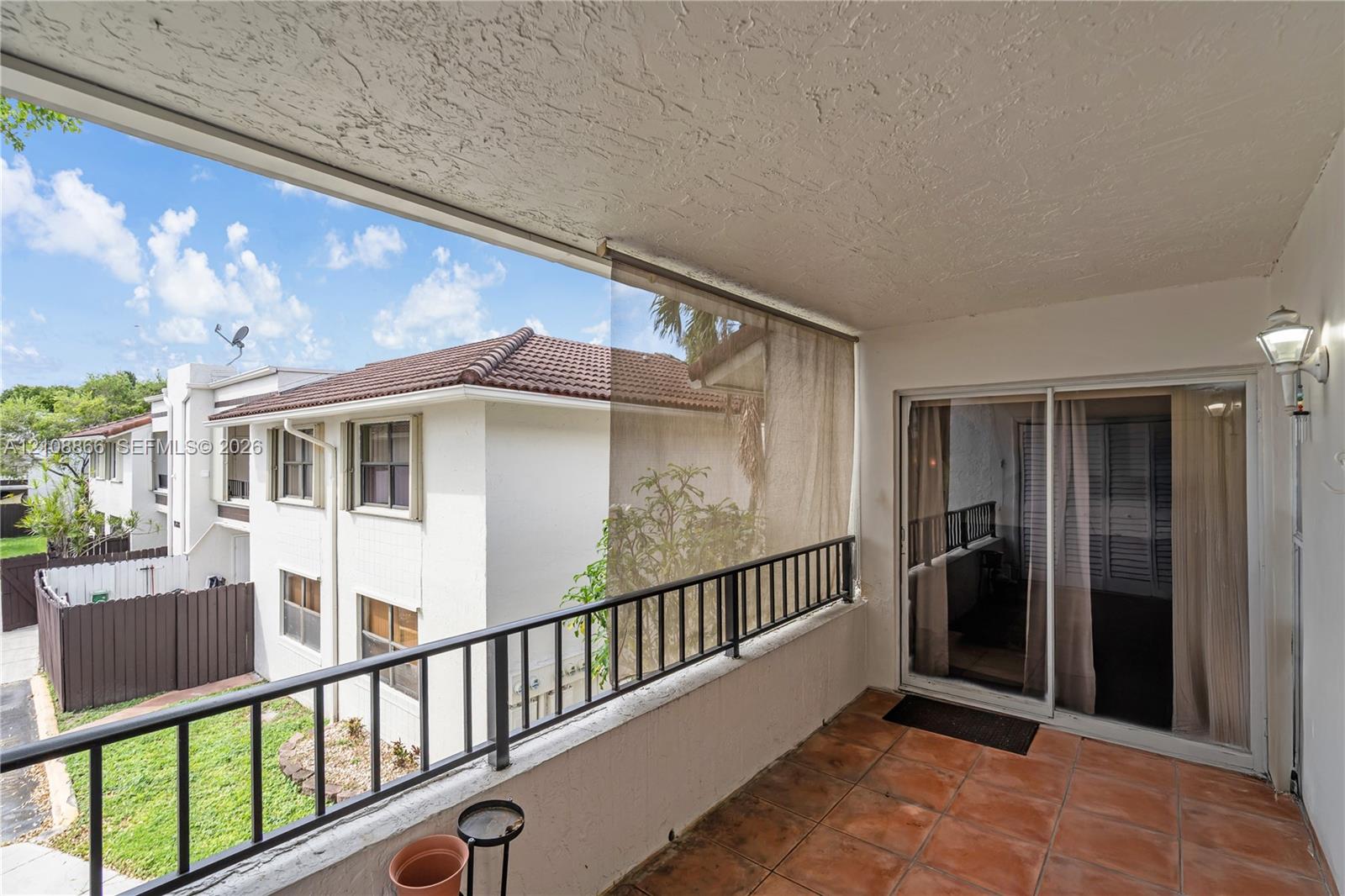 Covered balcony featuring terracotta-style tile flooring, metal railing, integrated wall-mounted exterior lighting, and sliding glass entry doors