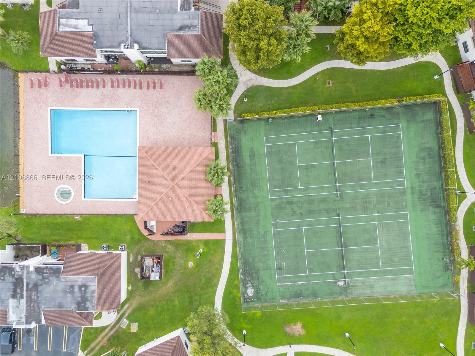 Community amenities featuring two full-sized tennis courts, an L-shaped swimming pool with an attached spa, a paved pool deck, and landscaped green space