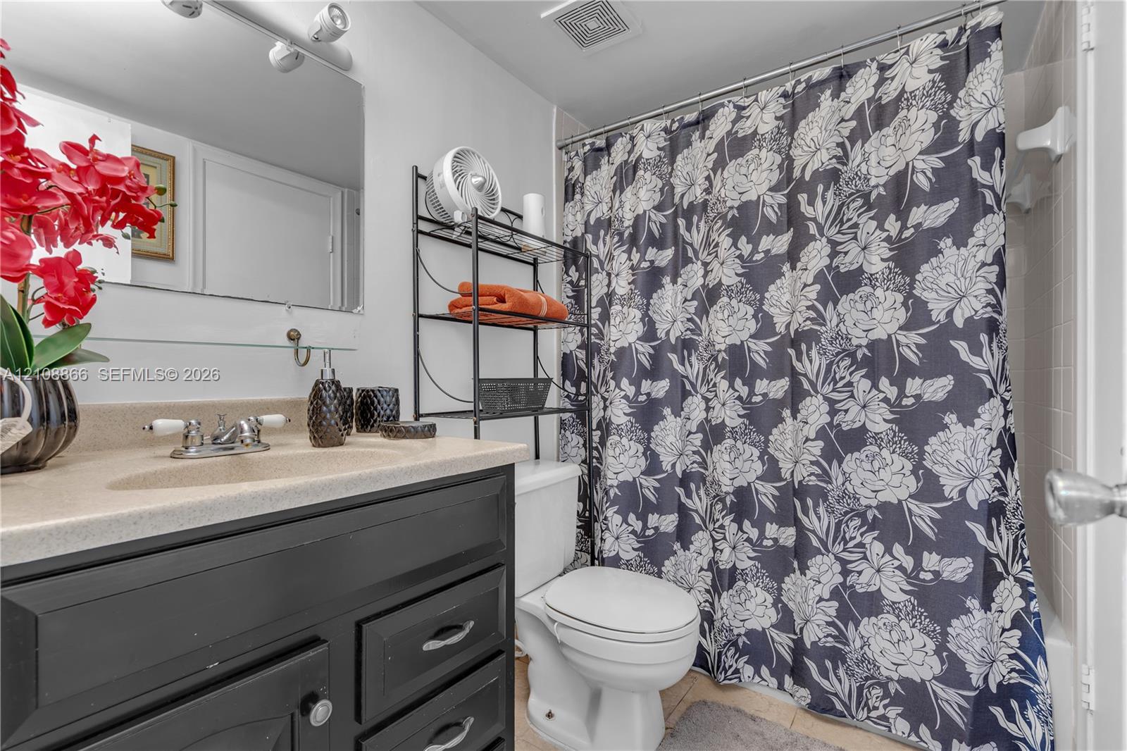 Bathroom featuring a black vanity with a molded countertop and integrated sink, chrome dual-handle faucet, wall-mounted mirror, and a tiled tub enclosure