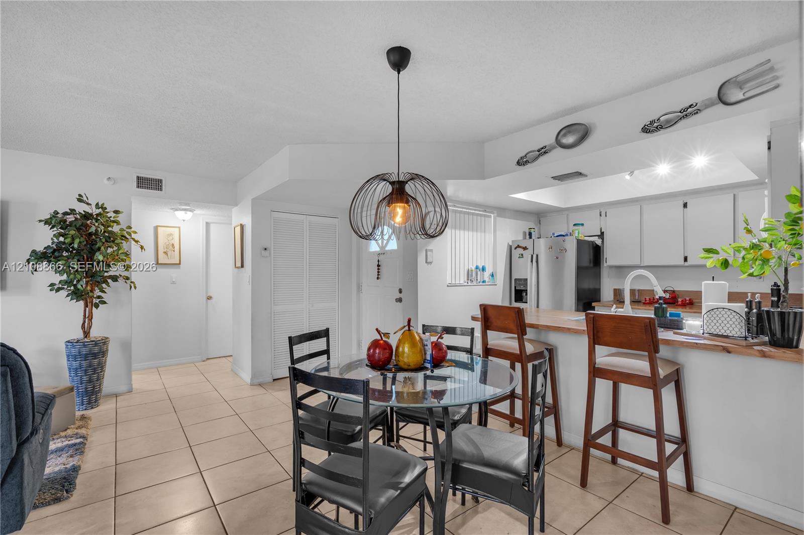 Open-concept kitchen featuring a breakfast bar with wood-finish countertop, white cabinetry, tile flooring, and a modern wire-frame pendant light