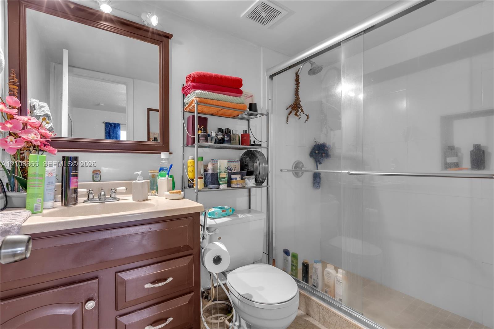 Bathroom featuring a dark wood-finish vanity, integrated sink, framed wall mirror, and a walk-in shower with a glass sliding door and built-in shelving niche