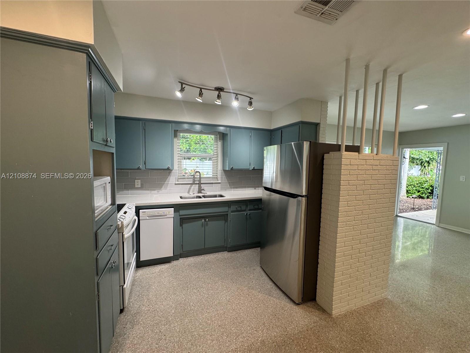Kitchen featuring blue cabinetry, stone-surface countertops, tile backsplash, stainless steel appliances, and a white brick partition wall