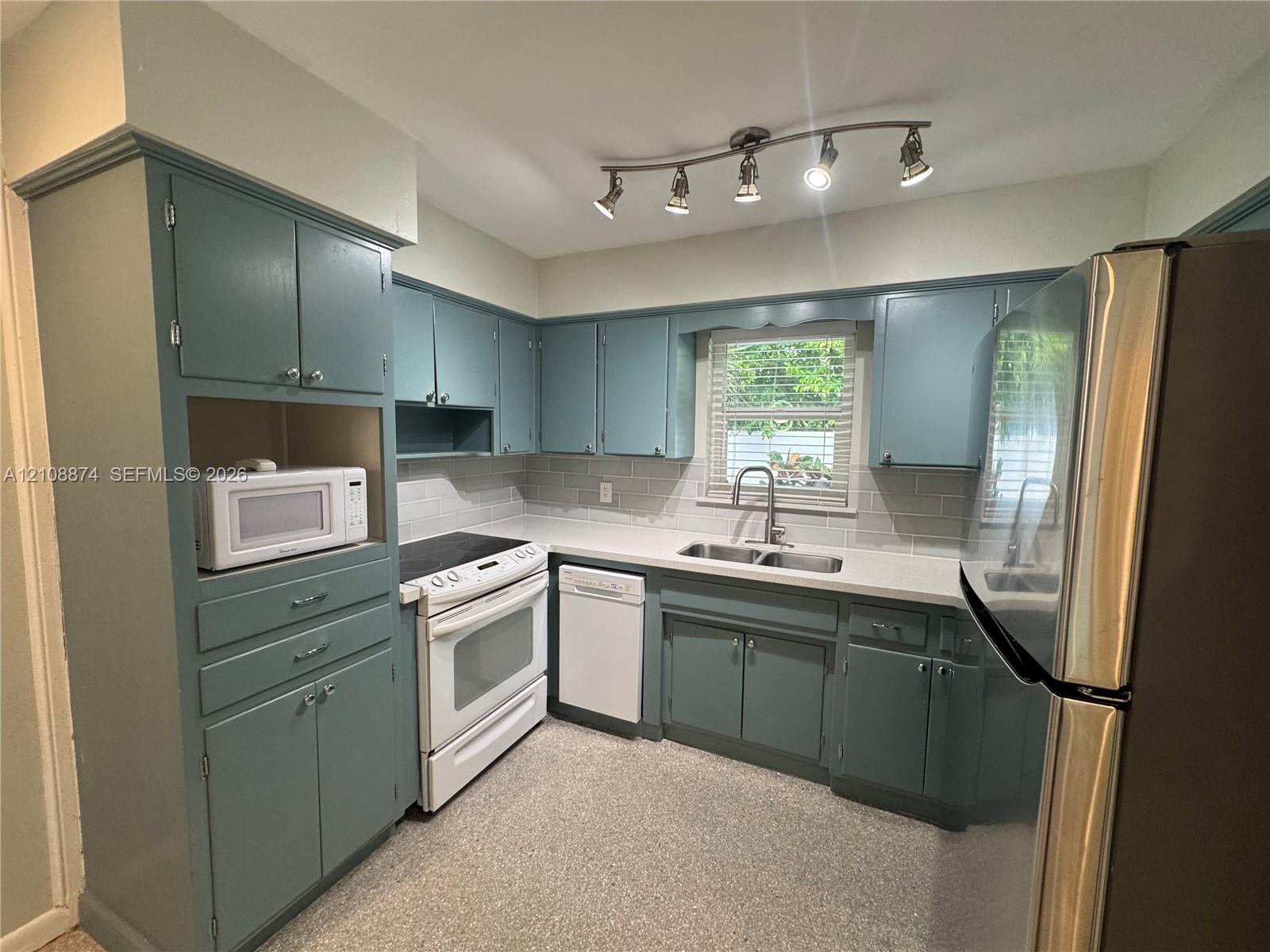Kitchen featuring painted cabinetry, subway tile backsplash, solid surface countertops, dual-basin stainless steel sink with pull-down faucet, and adjustable multi-light track lighting