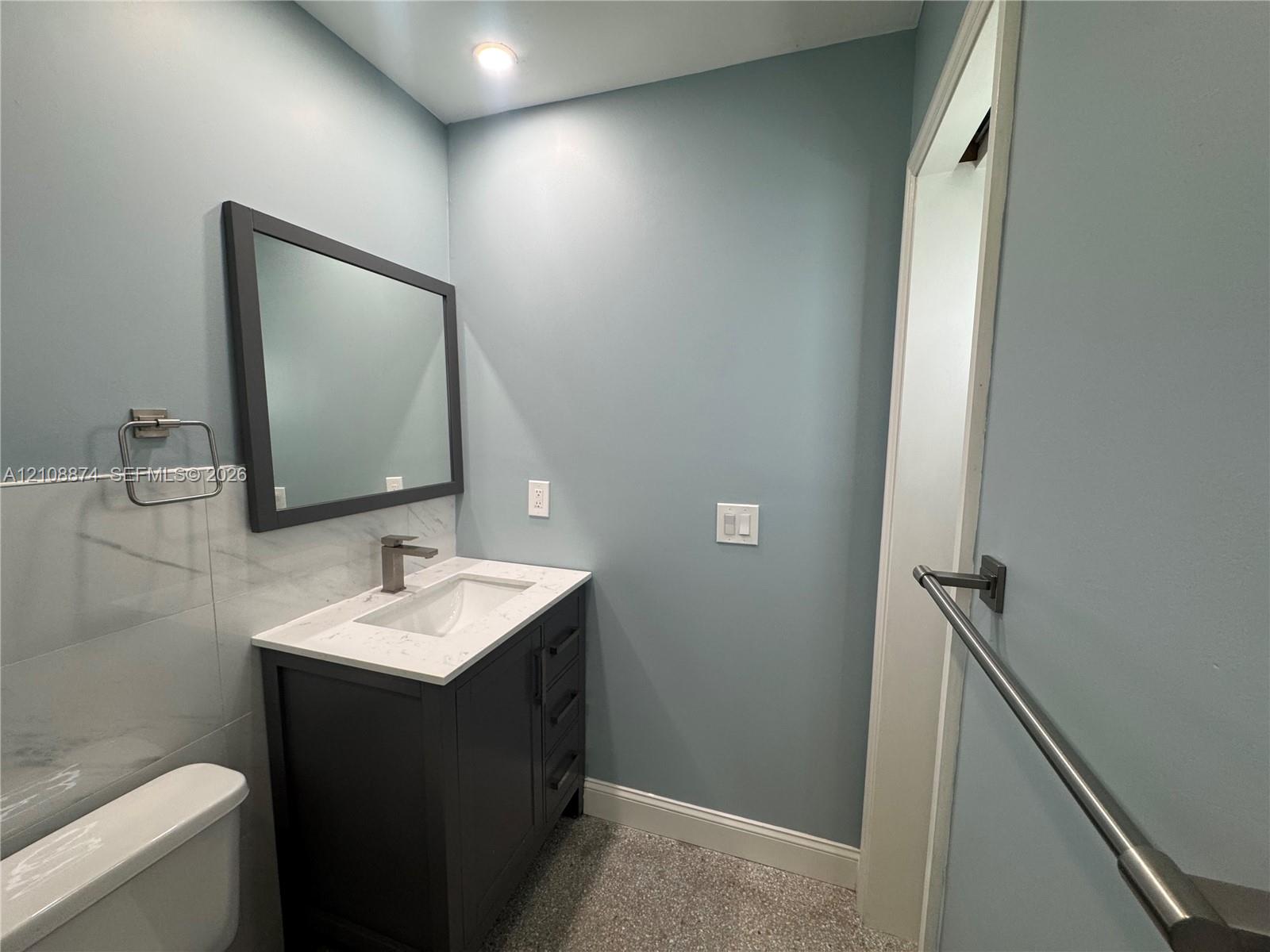 Vanity with a solid surface countertop, undermount sink, dark-finish cabinetry, framed wall mirror, and metal wall-mounted hardware