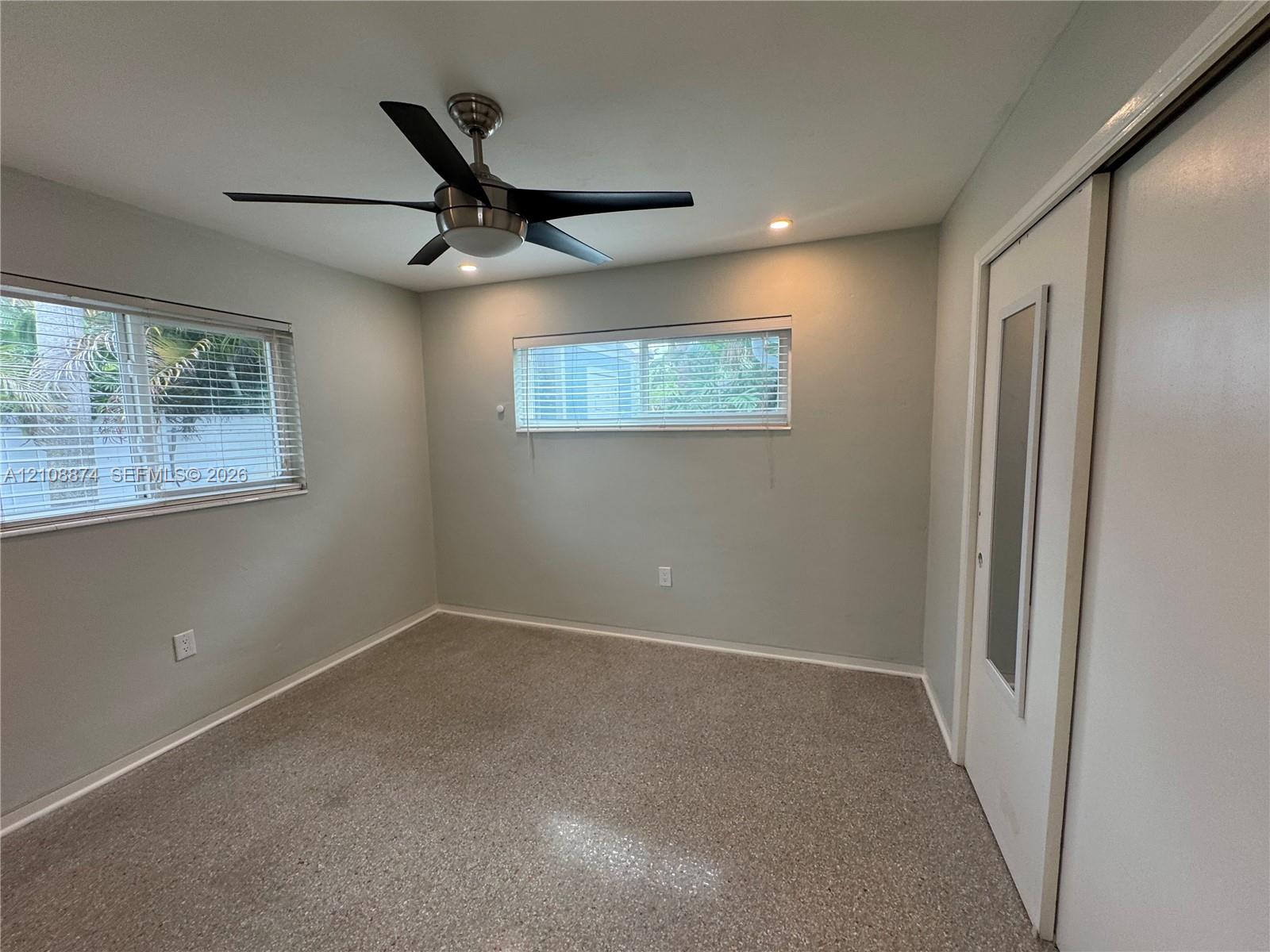 Neutral-toned room featuring a five-blade brushed metal ceiling fan, recessed lighting, horizontal slider windows, and a closet with a glass-paneled door
