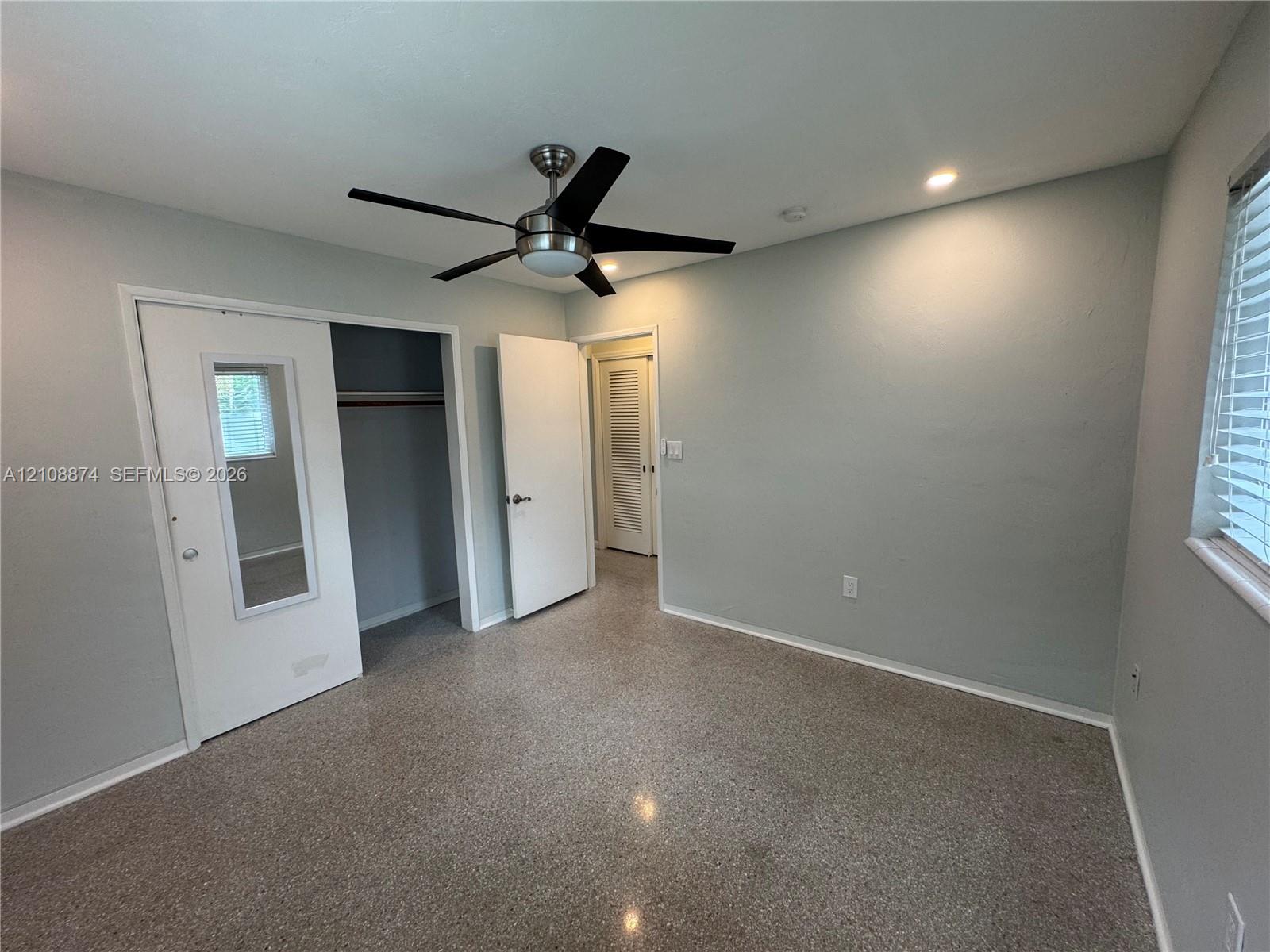 Neutral-toned interior featuring terrazzo flooring, a multi-blade ceiling fan with integrated lighting, recessed ceiling lights, and a closet with a mirrored door panel