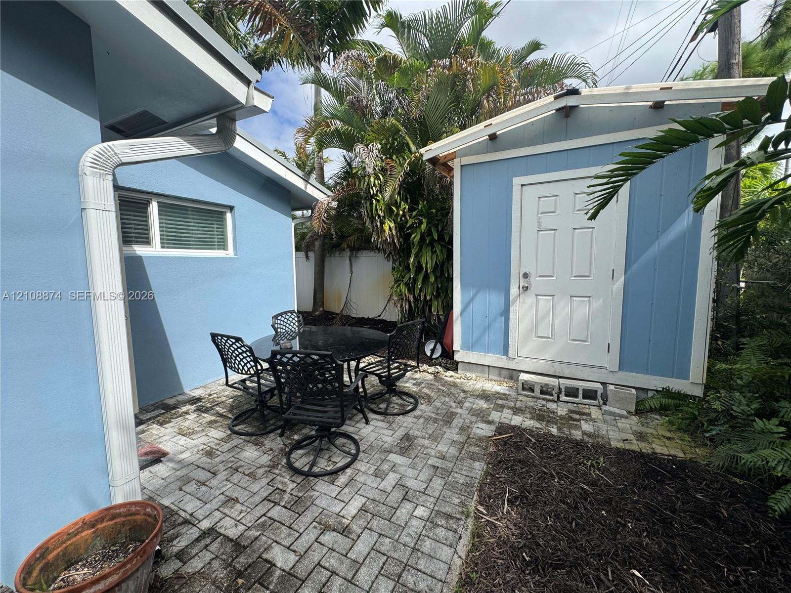 Paver patio featuring a standalone storage structure and mature landscaping