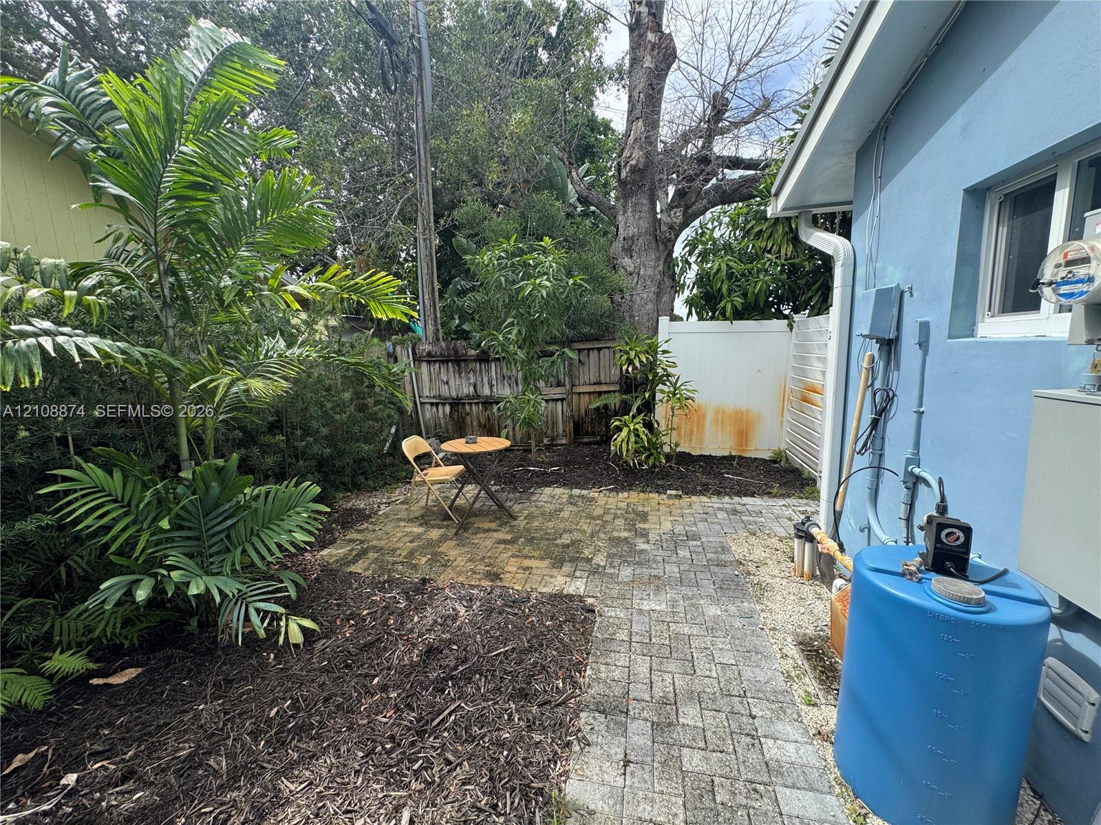 Outdoor space featuring a paved stone patio, mature landscaping with palm trees, and perimeter fencing