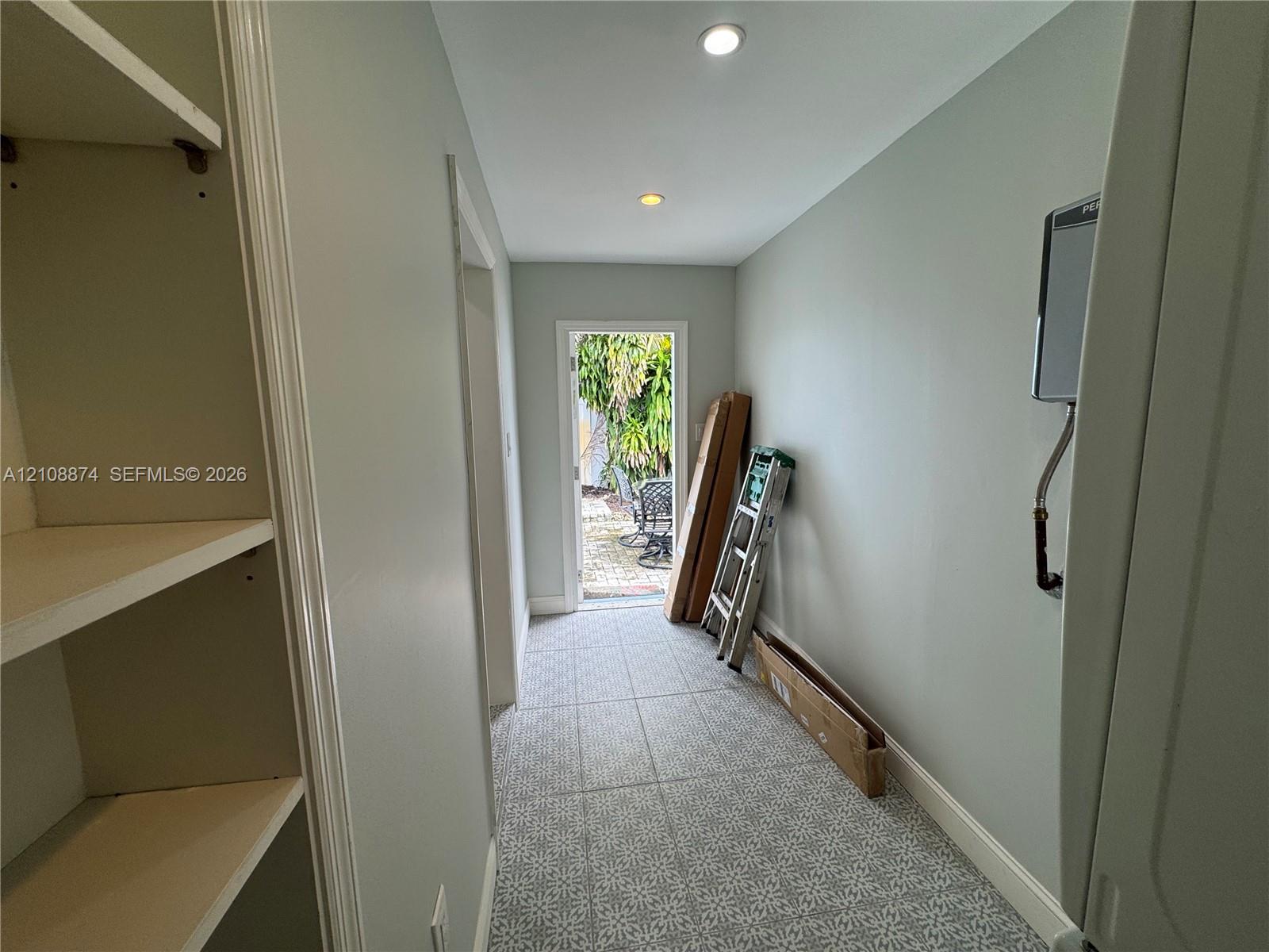 Hallway featuring patterned tile flooring, built-in shelving, recessed ceiling lighting, and a doorway providing egress to the exterior
