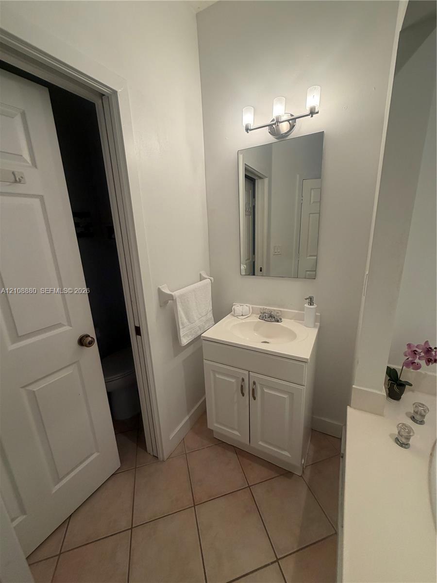 White vanity cabinet with an integrated sink basin, wall-mounted three-light fixture, rectangular frameless mirror, and neutral tile flooring