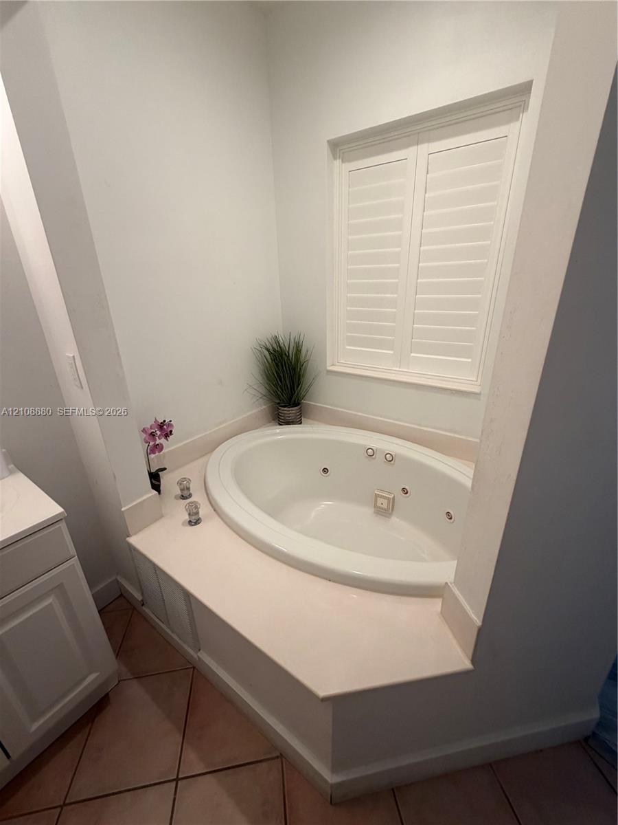Recessed soaking tub featuring a tiled deck surround and interior jets, accompanied by plantation shutters and ceramic tile flooring