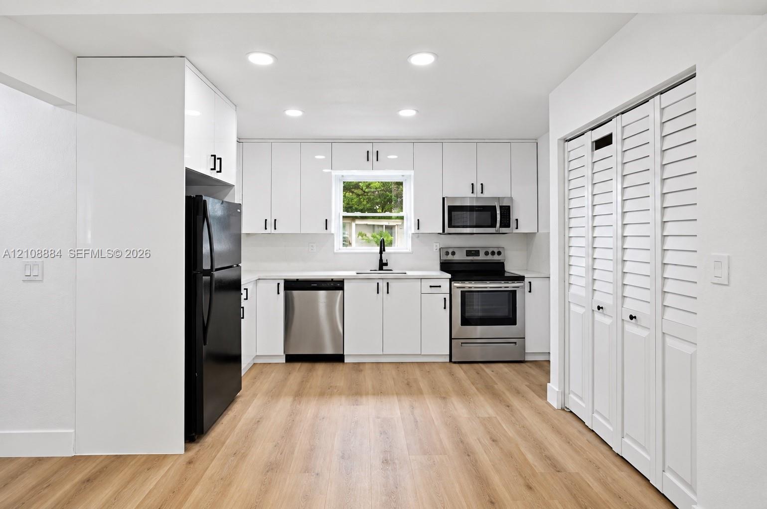 Kitchen featuring white shaker-style cabinetry, wood-finish flooring, recessed lighting, stainless steel appliances, and bi-fold louvered closet doors
