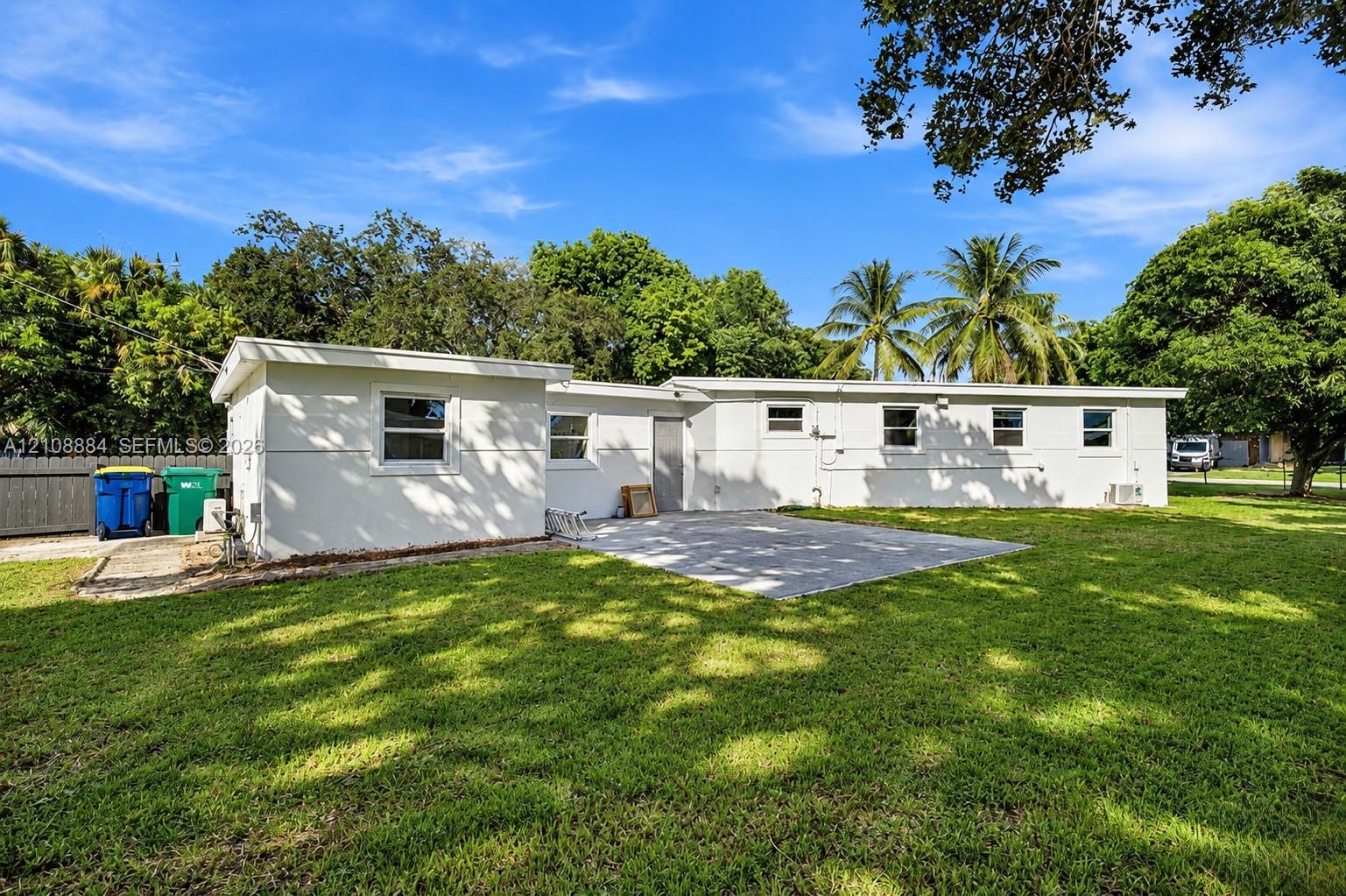 Exterior of the residence featuring a concrete patio, light-colored smooth finish siding, and mature trees on the grounds