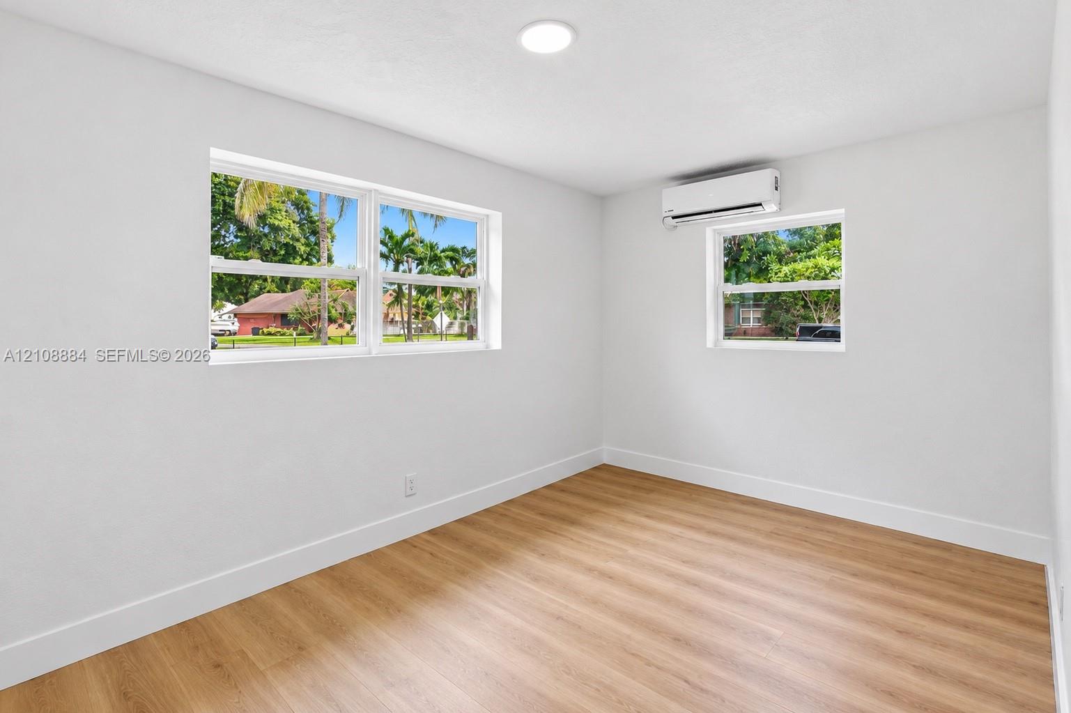 Room featuring wood-finish flooring, dual-aspect windows, and a wall-mounted ductless air conditioning unit