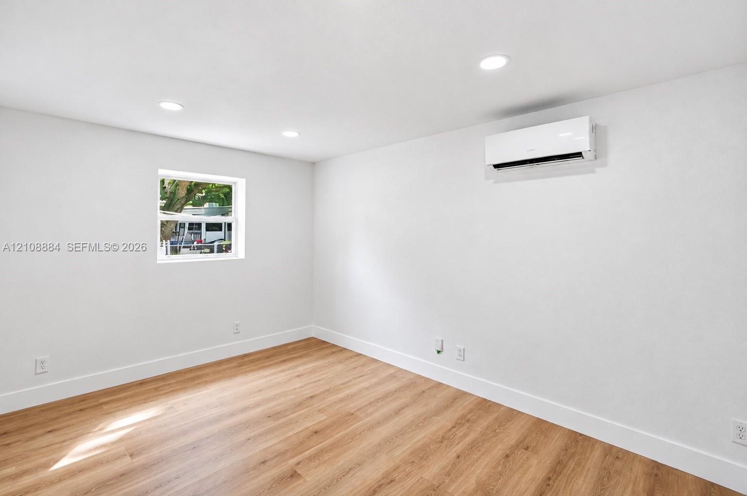 Room featuring wood-finish flooring, recessed lighting, neutral wall finishes, a wall-mounted ductless mini-split HVAC unit, and a single window