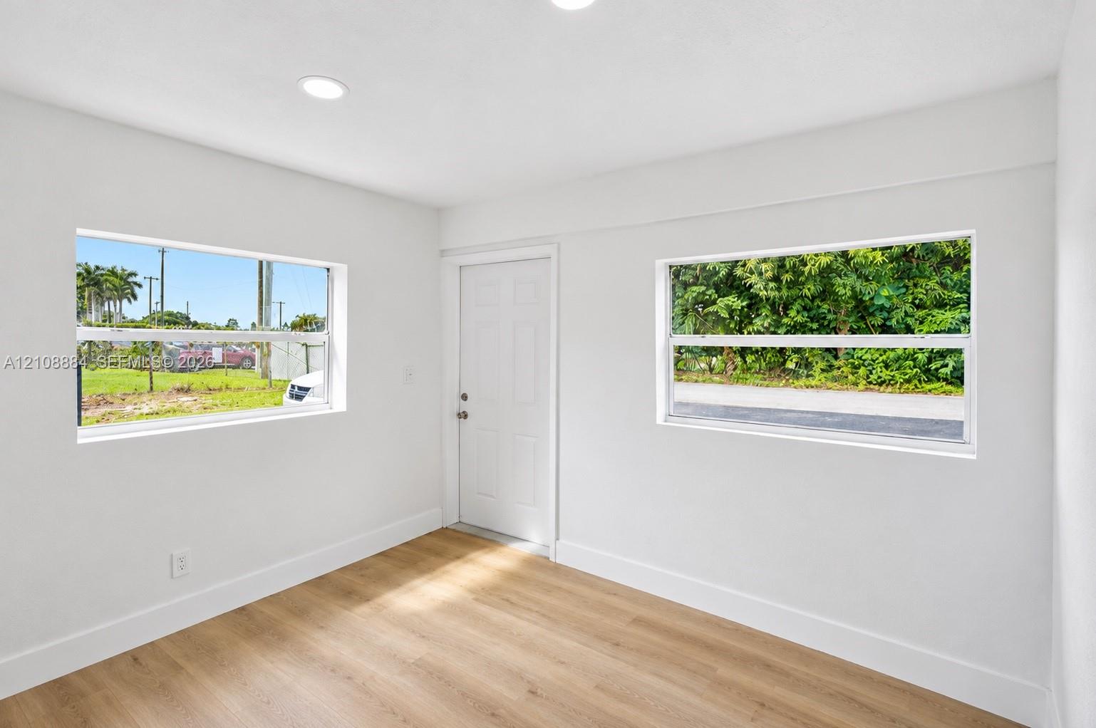 Interior space featuring wood-finish flooring, white walls, recessed ceiling lighting, two horizontal slider windows, and a solid-core entry door