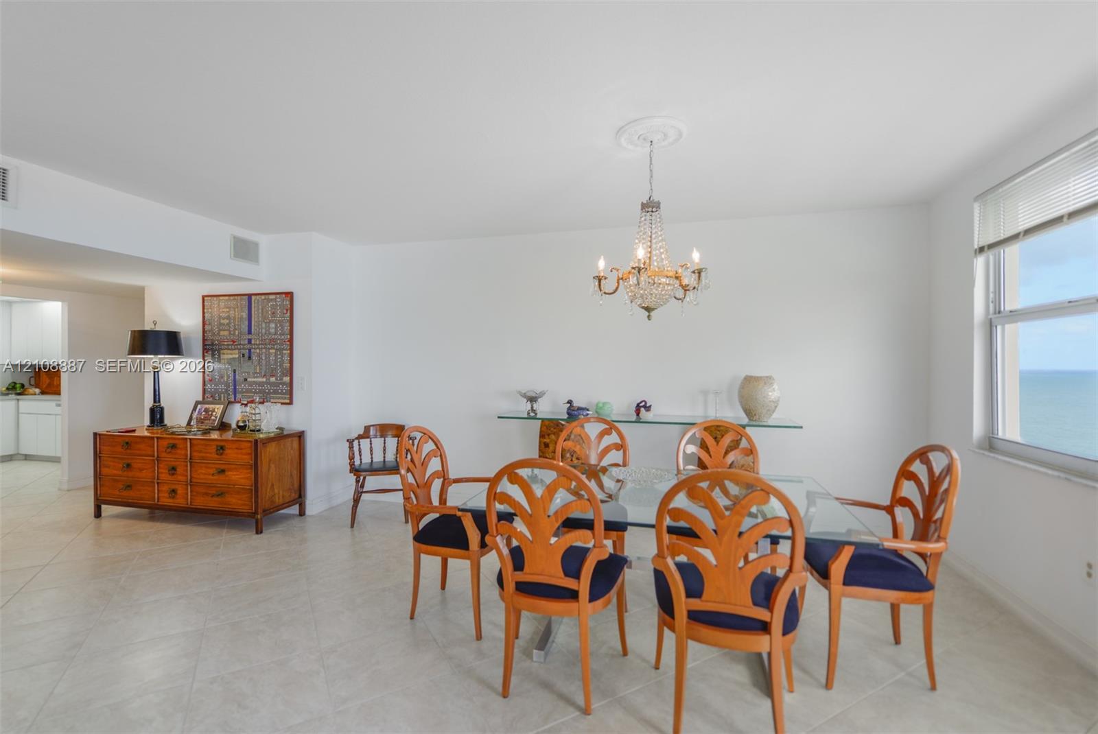 Open-concept living space featuring large-format tile flooring, a decorative crystal chandelier with ceiling medallion, and oversized windows providing an expansive water horizon