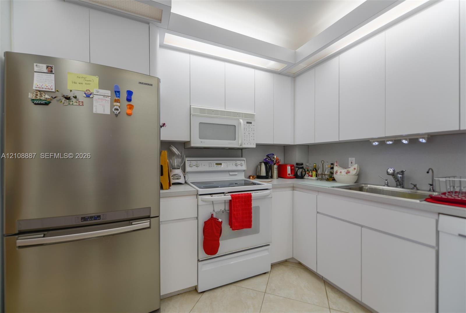 Kitchen featuring floor-to-ceiling white cabinetry, integrated recessed lighting, stainless steel refrigerator, white electric range with over-the-range microwave, and tile flooring