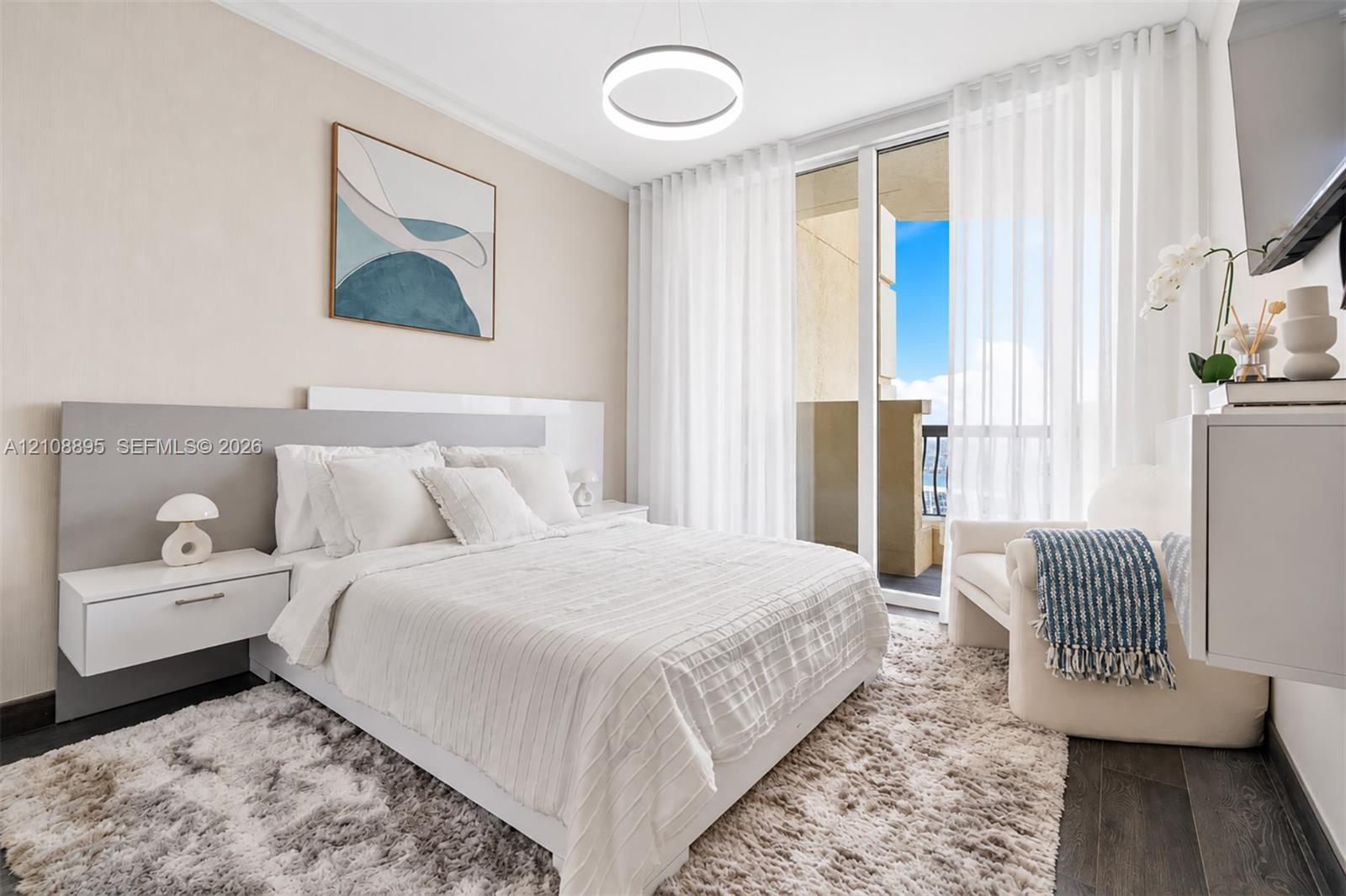 Floor-to-ceiling glass sliding doors with balcony access, wood-finish flooring, integrated wall-mounted nightstands, circular pendant lighting, and a neutral-toned accent headboard panel