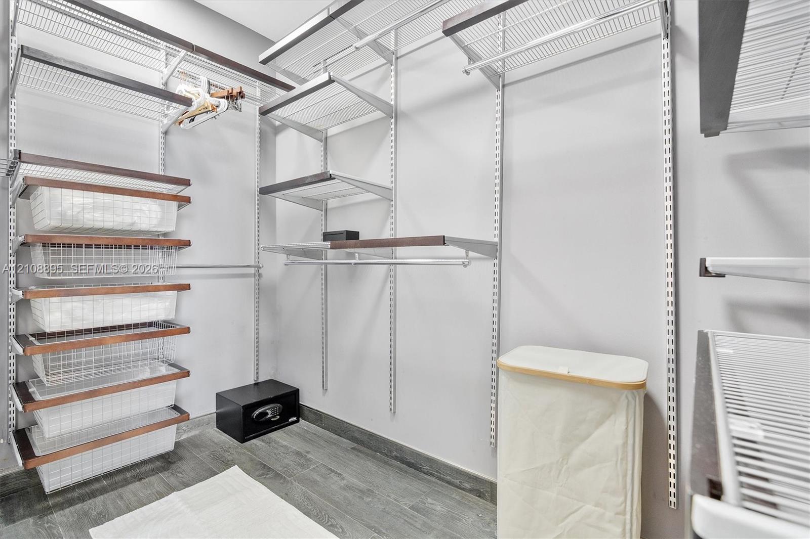 Walk-in closet featuring floor-to-ceiling metal shelving units, integrated wire basket organizers, wood-finish shelving accents, and wood-finish flooring