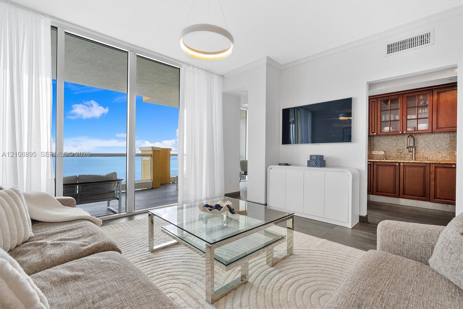 Floor-to-ceiling glass sliding doors, private balcony, wood-finish flooring, built-in wet bar with cabinetry, and modern circular pendant lighting