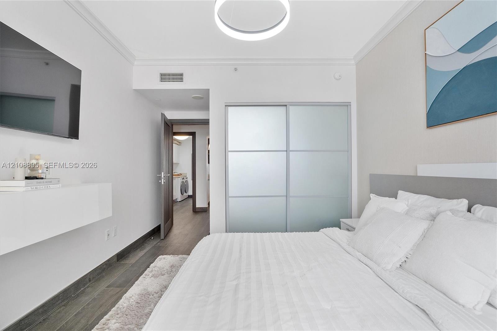 Wood-finish flooring, sliding frosted-glass closet doors, wall-mounted floating shelf, and contemporary circular overhead lighting