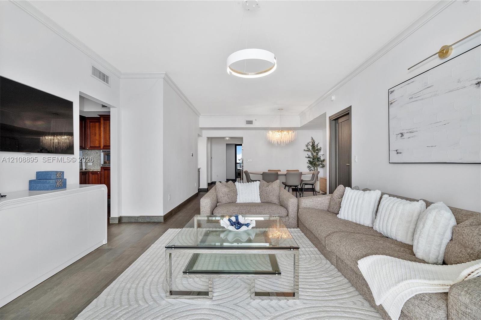 Open-concept living space featuring wood-finish flooring, crown molding, a circular modern pendant light, and a multi-tiered crystal chandelier