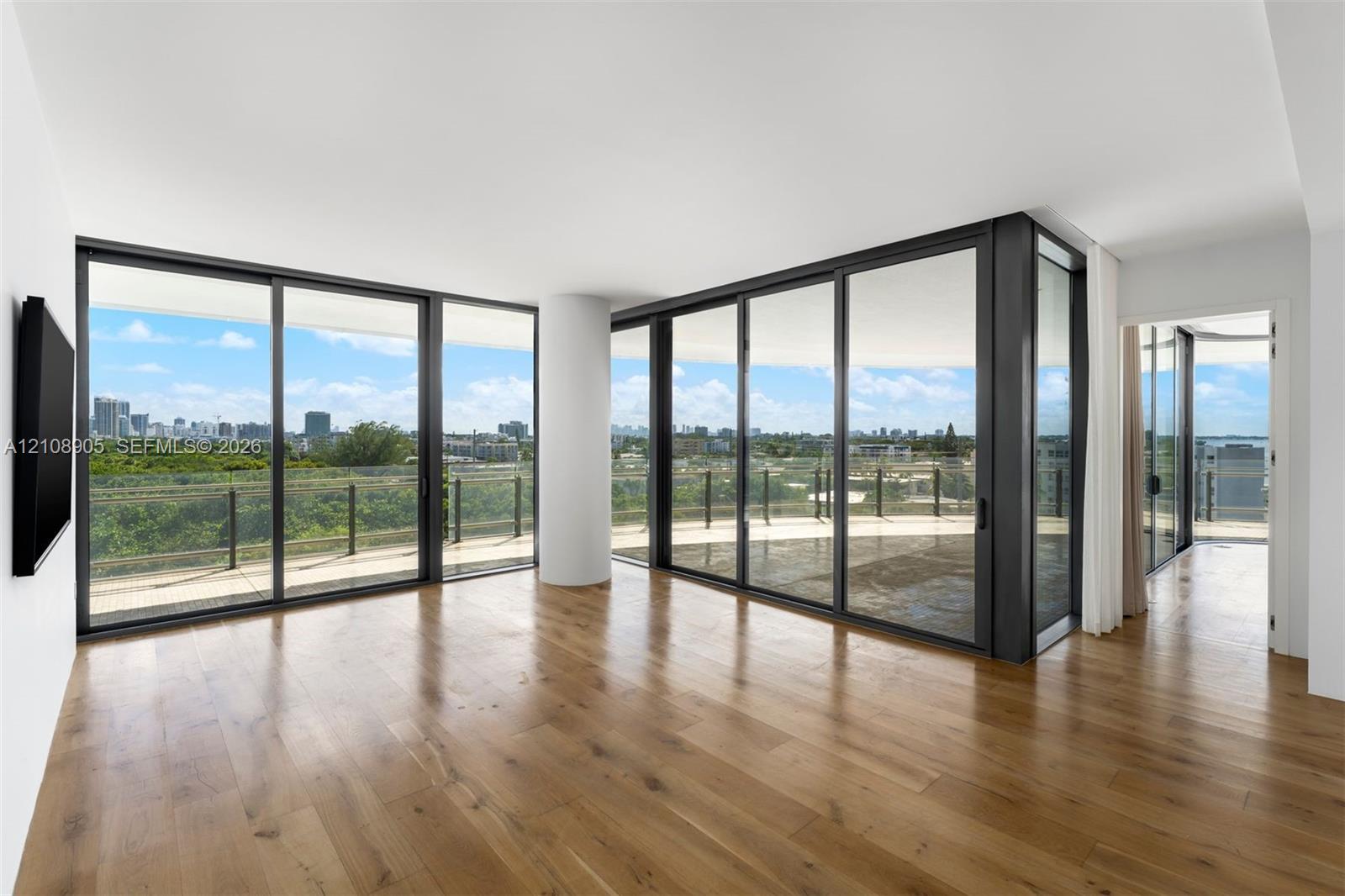 Floor-to-ceiling glass sliding doors, wood-finish flooring, and a wrap-around balcony with industrial-style metal railing