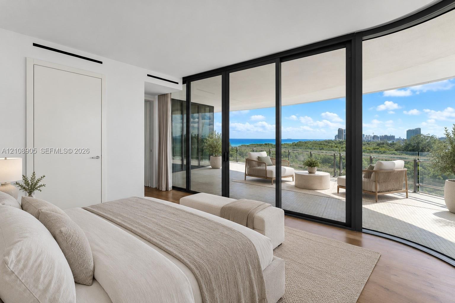 Floor-to-ceiling retractable glass walls, wide-plank wood flooring, expansive private balcony, recessed linear lighting, and coastal landscape backdrop