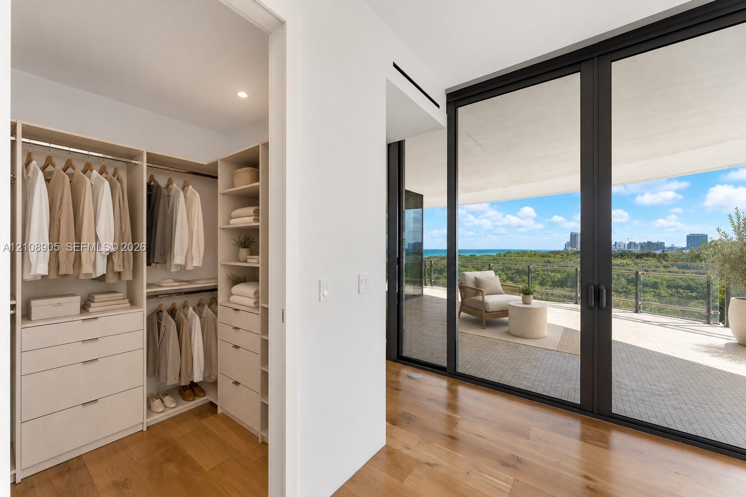 Built-in closet system with integrated shelving and drawer storage, wood-finish flooring, and expansive floor-to-ceiling glass doors opening to a covered balcony with a glass railing