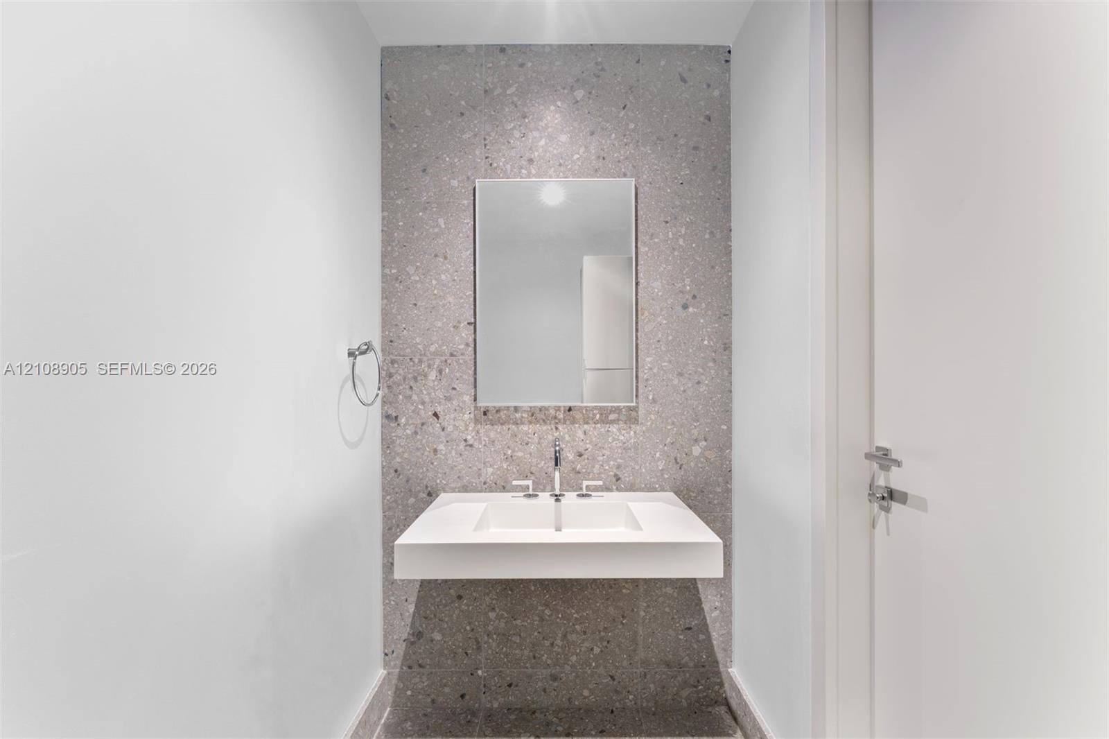Floating vanity featuring an integrated rectangular sink, wall-mounted faucet, full-height terrazzo tile accent wall, and a framed mirror