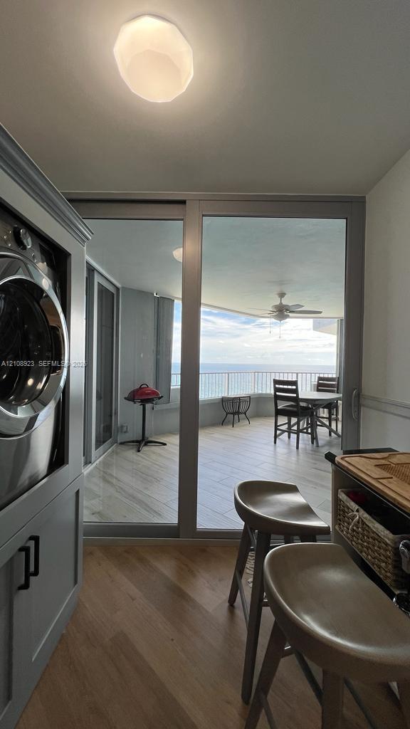 Built-in laundry cabinetry with integrated washer, wood-finish flooring, floor-to-ceiling sliding glass doors, and expansive covered balcony with tile flooring