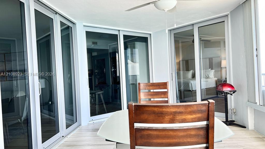 Enclosed sunroom featuring light-toned tile flooring, white-finished ceiling, multi-panel sliding glass doors, and a ceiling-mounted fan
