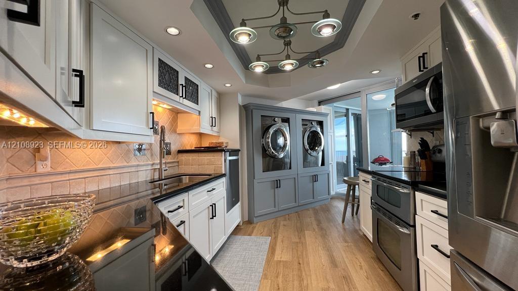 Kitchen featuring custom cabinetry, dark stone countertops, built-in stainless steel appliances, integrated laundry area with dual units, and recessed lighting with a decorative ceiling fixture