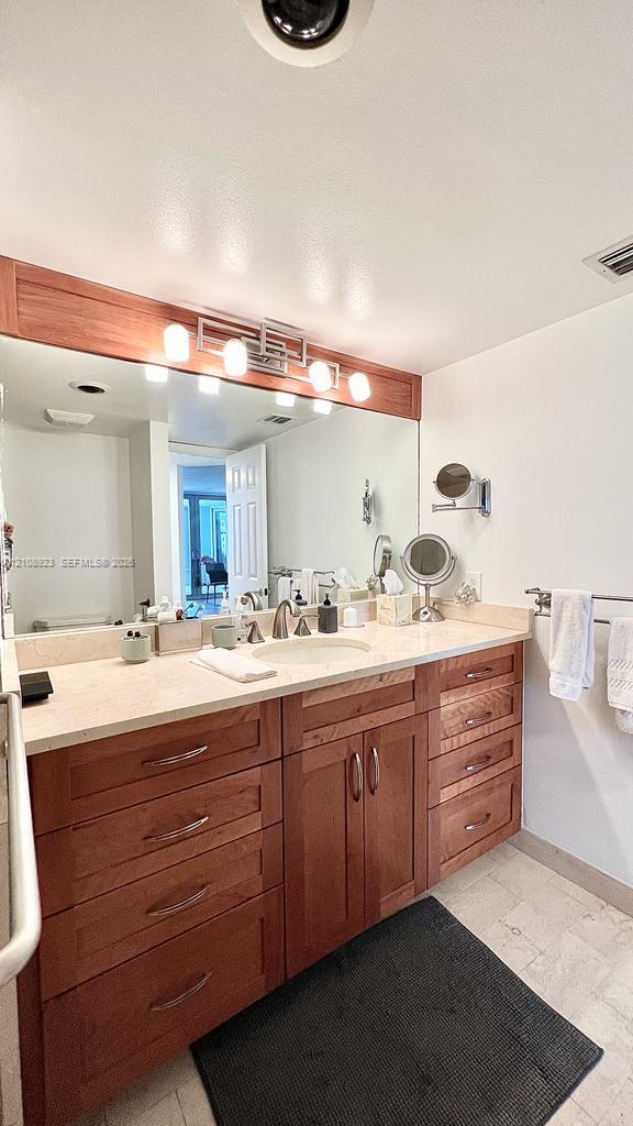 Wood-finish vanity cabinetry with multiple storage drawers, light-toned countertop featuring an integrated sink, expansive mirror, and a wall-mounted multi-bulb light fixture