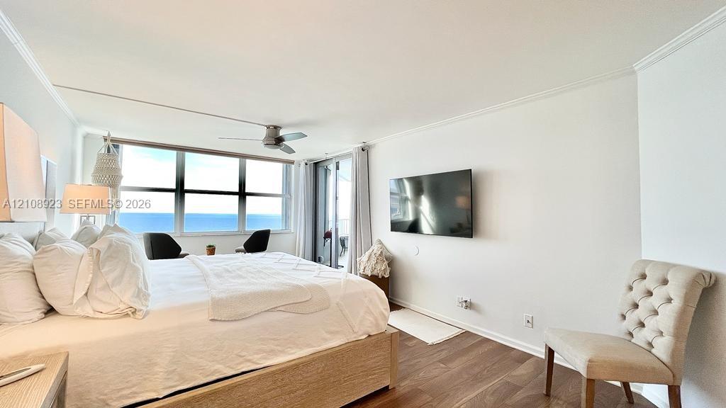 Bedroom featuring wood-finish flooring, ceiling fan, crown molding, and large-format window panels with ocean scenery