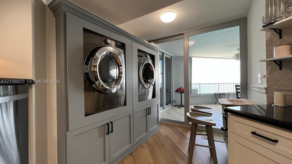 Built-in cabinetry featuring recessed-panel doors and matte black hardware, integrated laundry appliances, wood-finish flooring, and floor-to-ceiling glass sliding doors