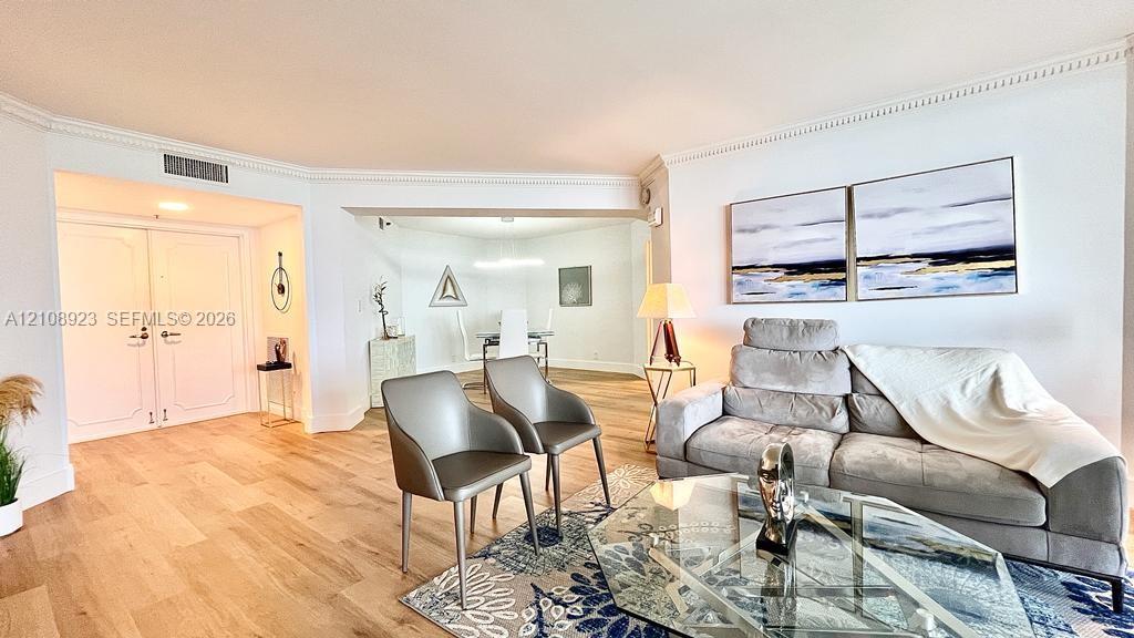 Open-concept interior featuring light wood-finish flooring, crisp crown molding, and double-door entry